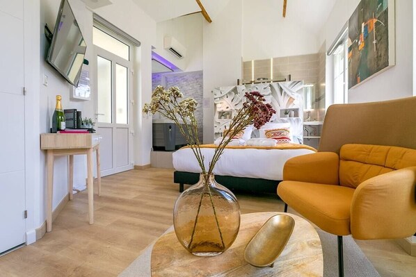 A modern hotel room with a bed, a sofa, a TV, and a vase with flowers.