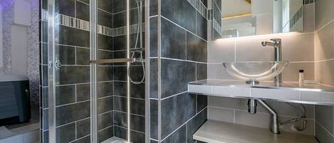 Een moderne badkamer met een douche met glazen wand, een wastafel op een zuil en een grote spiegel.