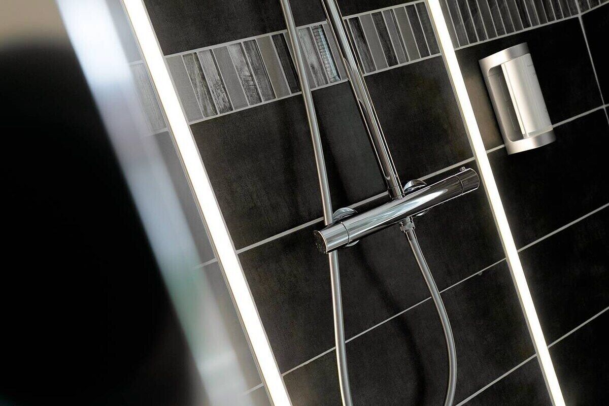 A modern bathroom with a black tiled wall, a chrome showerhead, and a small, cylindrical object on the wall.