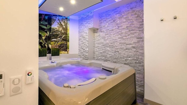 Ein modernes Badezimmer mit Whirlpool, Steinwand und Blick auf tropische Pflanzen.