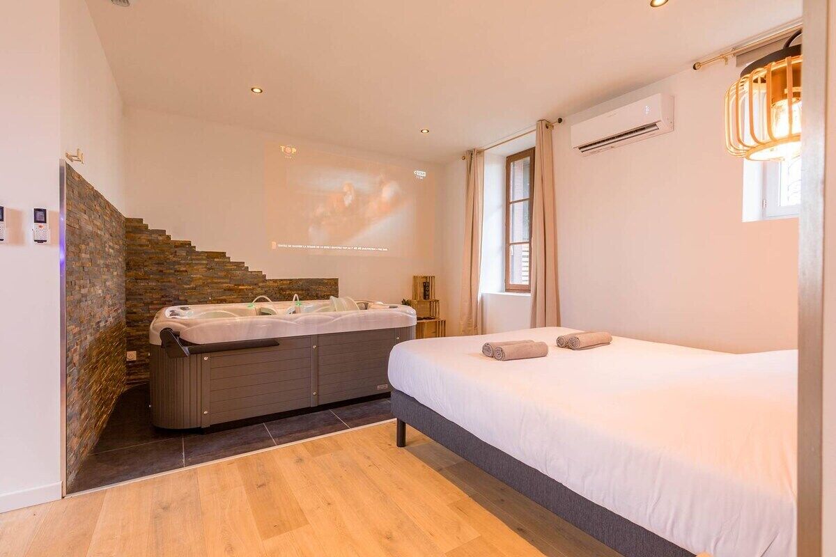 A bedroom with a bed, a hot tub, a staircase, and a projector screen.
