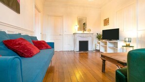 Un salón con un sofá azul, cojines rojos, una chimenea, un televisor y una mesa de madera.