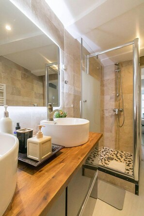A modern bathroom with a large white sink, a glass shower enclosure, and a wooden countertop. - Château Biek (Dijon)