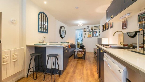 A compact kitchen with a central island, bar stools, a dishwasher, and a dining area with a sofa. - Château Biek (Dijon)