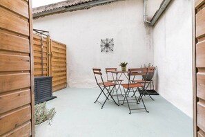 A wooden table with chairs in a courtyard, a metal wall decoration, and a wooden gate. - Château Biek (Dijon)