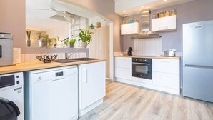 Una cocina moderna con armarios blancos, lavavajillas, horno, refrigerador y estufa integrada.