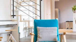 Una sala de estar moderna con un sillón azul, una escalera y un comedor.