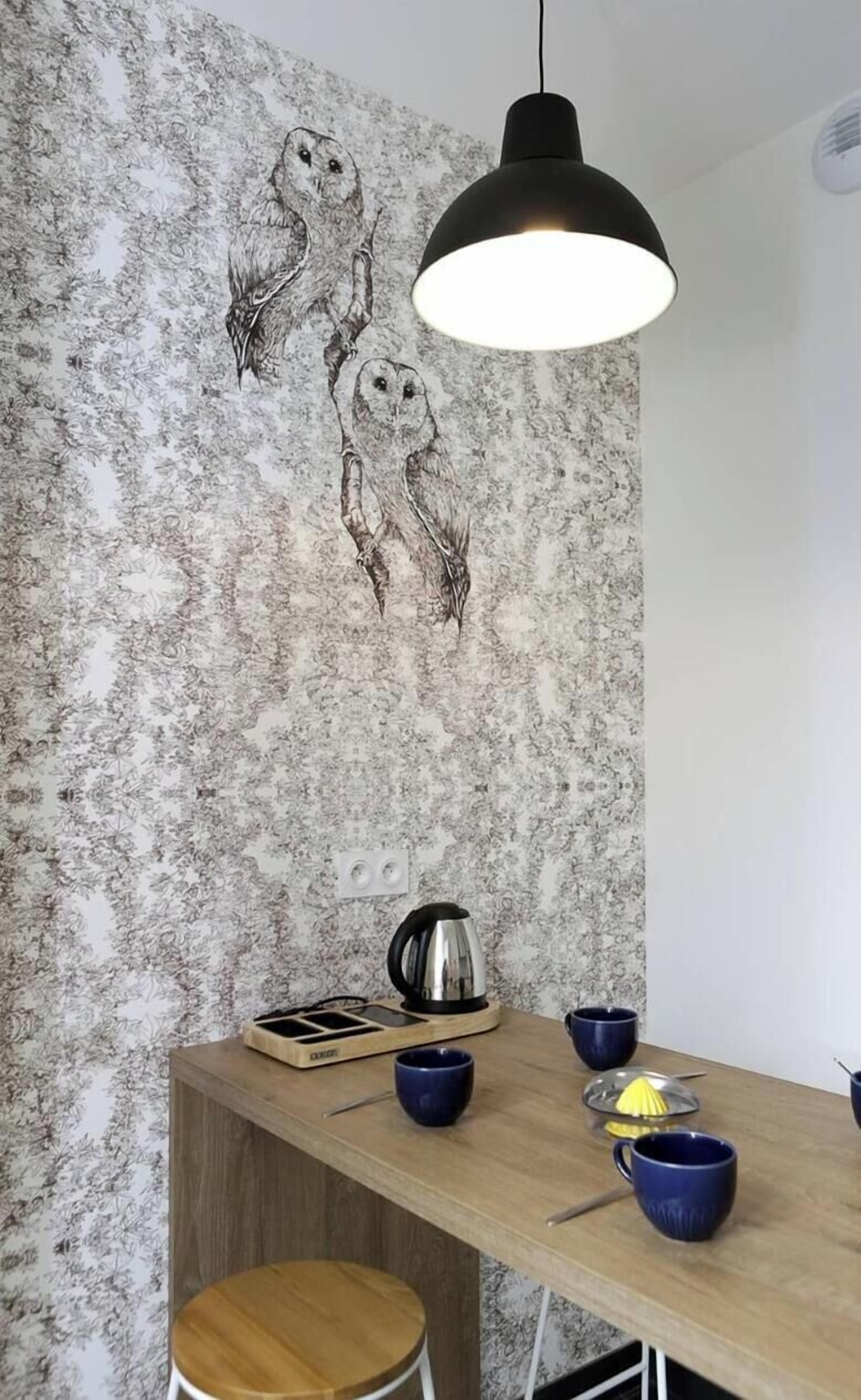 Un comedor con una mesa de madera, tazas azules, una tetera y una pared decorada con un mural de un búho.