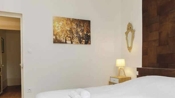 A hotel room with a bed, a painting, a lamp, and a mirror on the wall. - La Chouette –  Cité Gastronomique (Dijon)