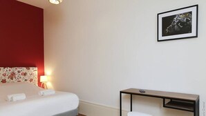 A hotel room with a bed, a desk, a chair, a lamp, and a framed picture on the wall. - La Chouette –  Cité Gastronomique (Dijon)