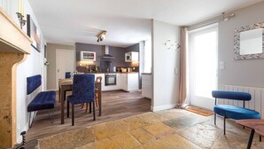 A modern kitchen with white cabinets, a central island, and a dining area with blue upholstered chairs. - Le Duplex des Ducs- Au cœur du centre Historique- (Dijon)