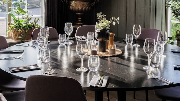 A dining area with a round table set for a meal, surrounded by chairs. - Hotell MAVI (Viken)