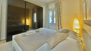Une chambre d’hôtel avec un grand lit, une armoire, un miroir, une fenêtre avec des rideaux et une lampe de chevet.