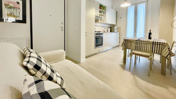Un espace de vie compact comprenant un canapé, une table à manger avec des chaises, un coin cuisine et une porte.