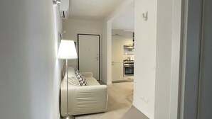 Un salon moderne et minimaliste, avec un canapé, une lampe sur pied et une porte donnant sur la cuisine.