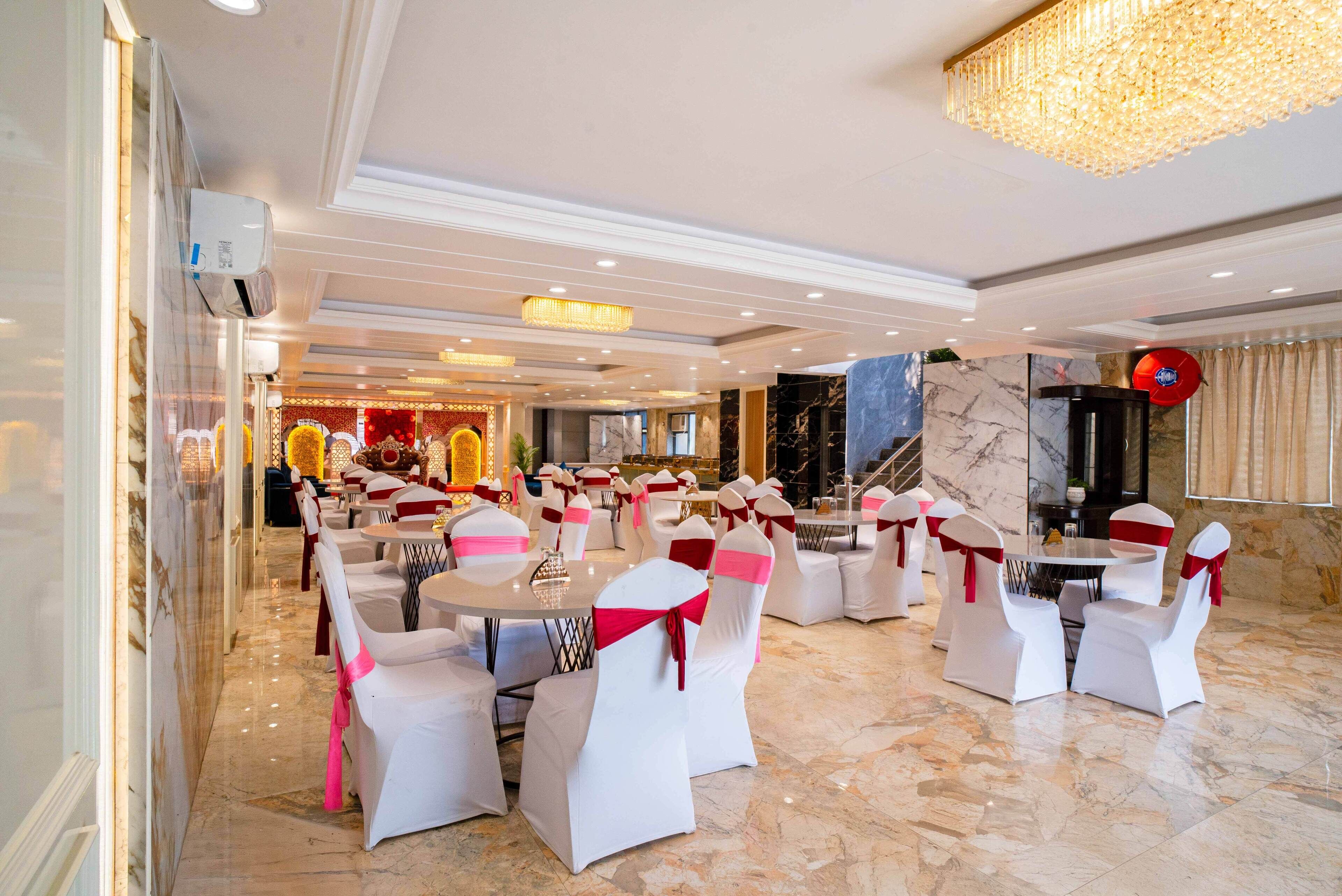 A banquet hall with round tables and white chairs, each with a red ribbon.