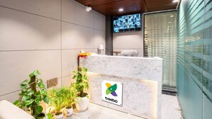 A reception area with a marble counter, potted plants, and a television screen displaying multiple images. - Treebo Royal Grand, Sector 71 (Noida)