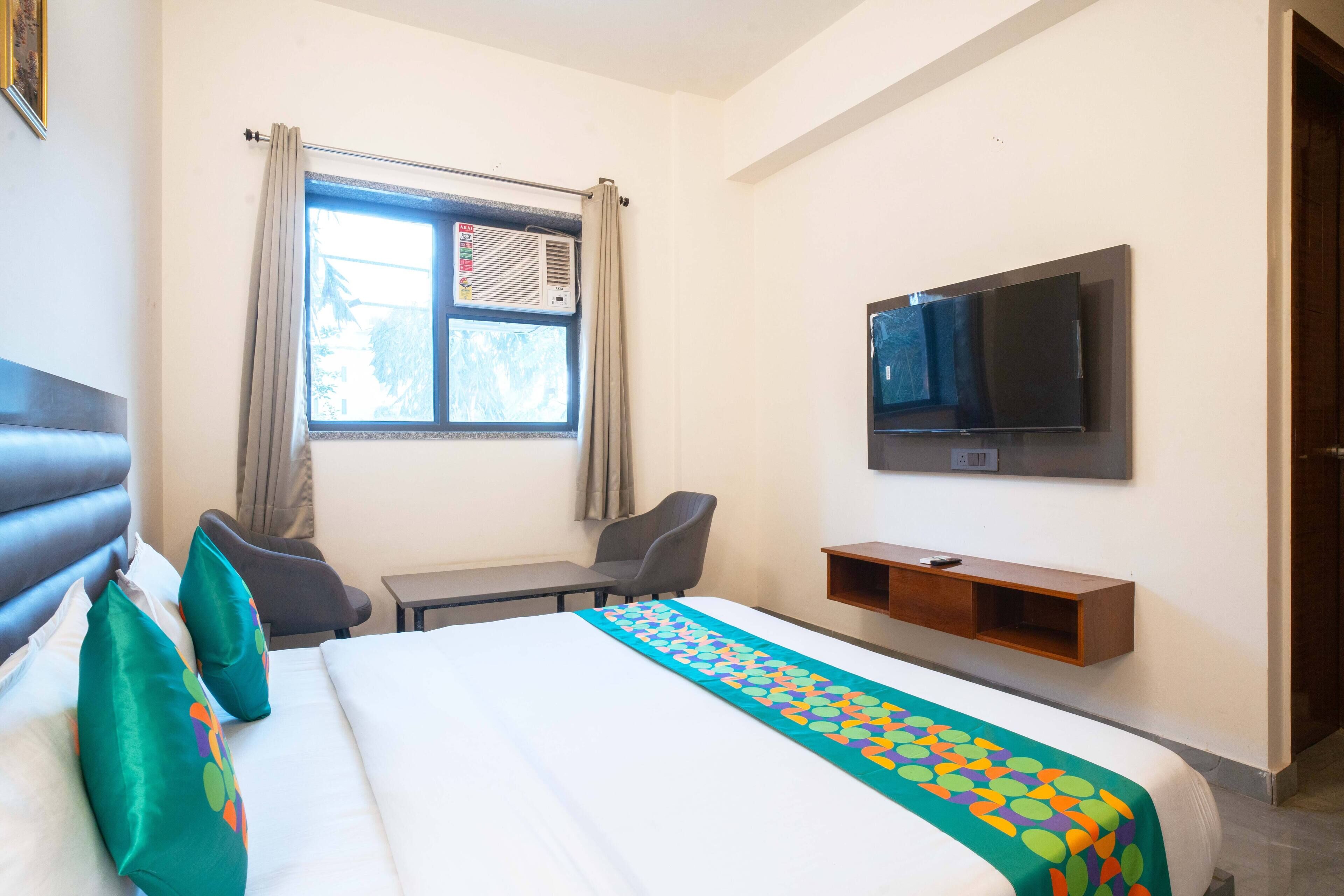 A hotel room with a bed, a desk, a chair, a TV, and a window with curtains.