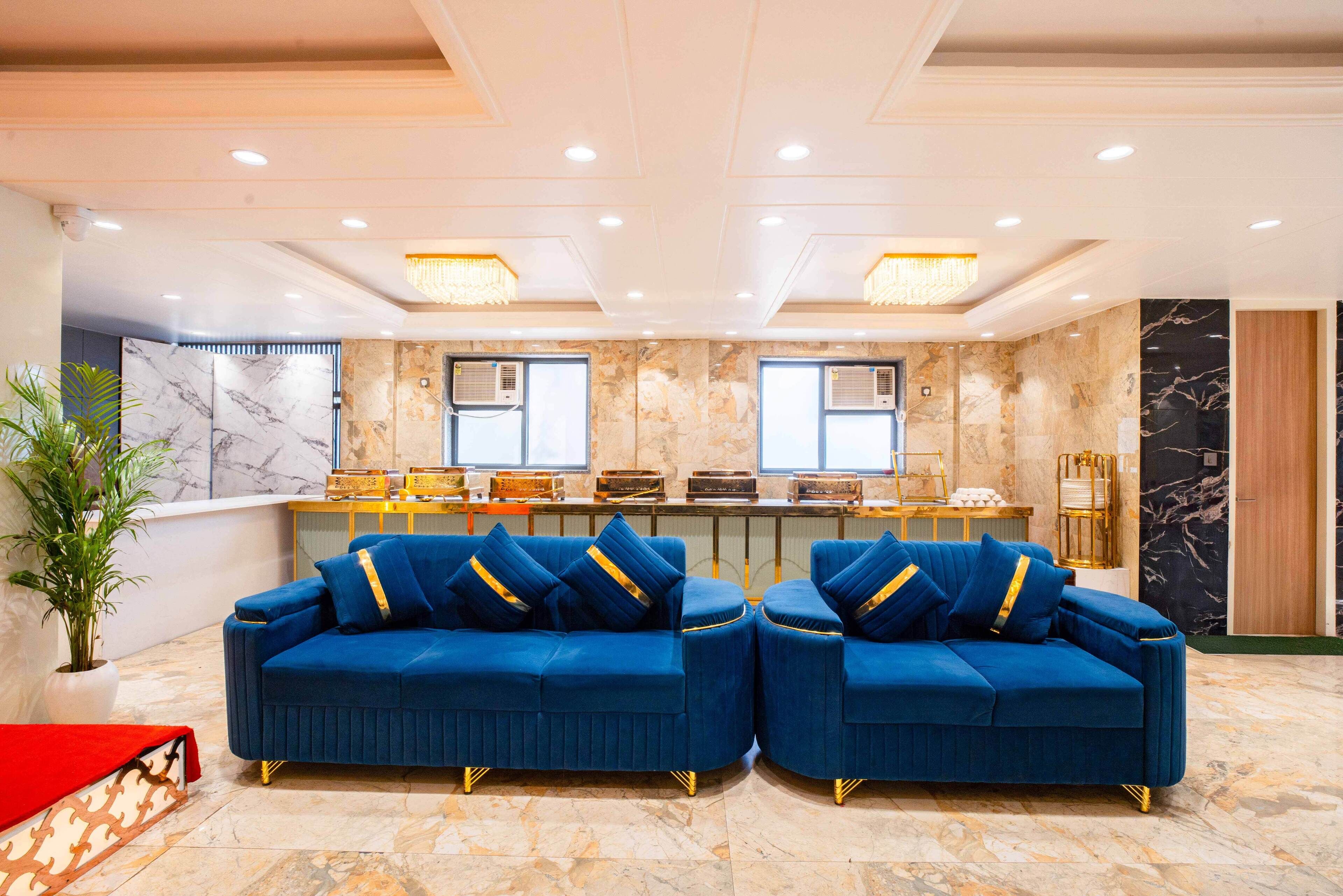 A lobby with two blue sofas, a marble reception desk, and a potted plant.