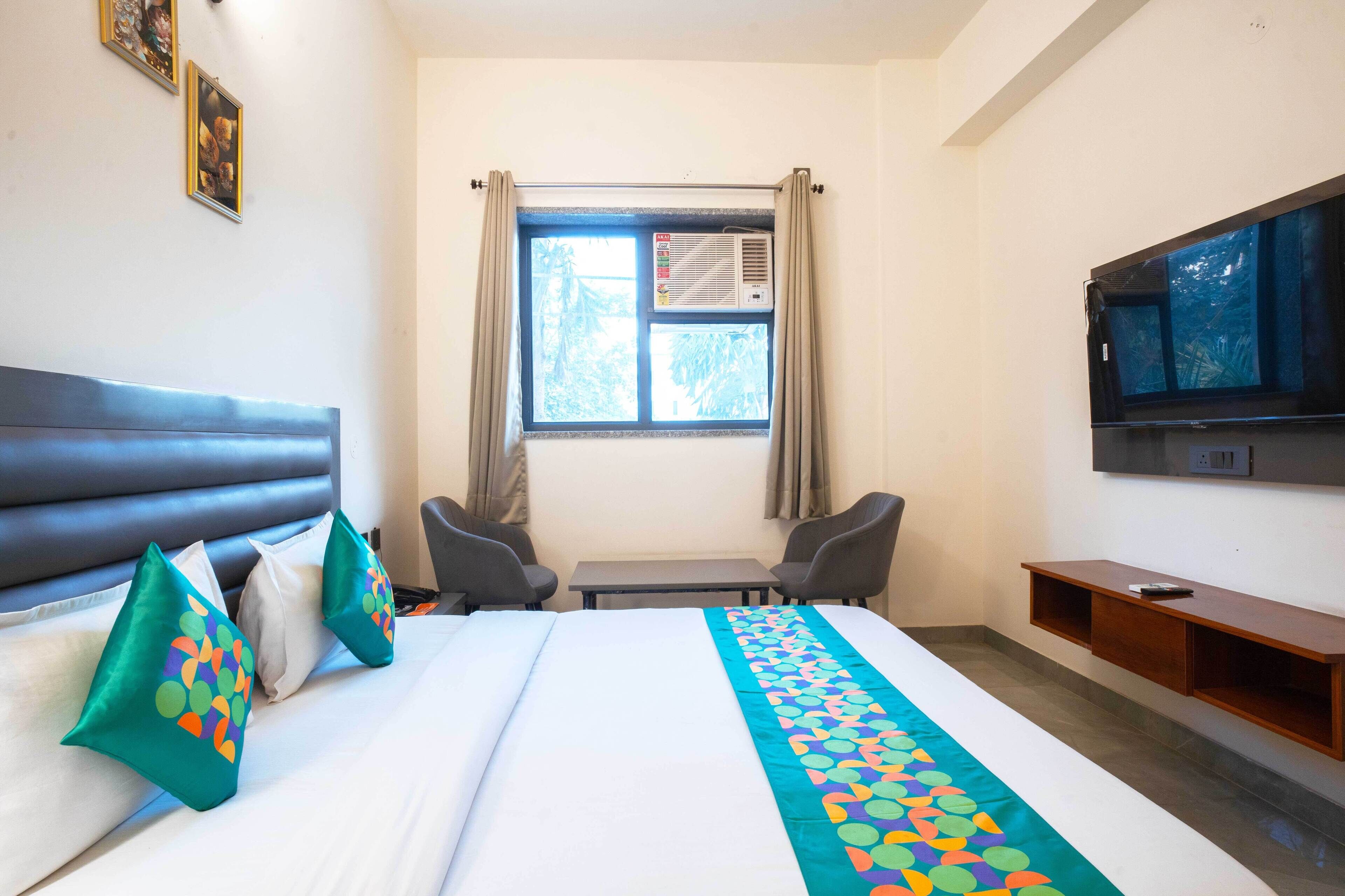 A hotel room with a bed, two chairs, a TV, and a window with curtains.