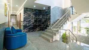 A modern lobby with a marble wall, a blue sofa, and a staircase. - Treebo Royal Grand, Sector 71 (Noida)