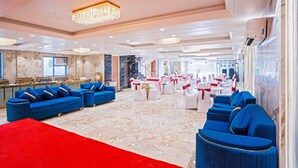A spacious hall with blue sofas, a red carpet, and white tables with red and white decorations. - Treebo Royal Grand, Sector 71 (Noida)