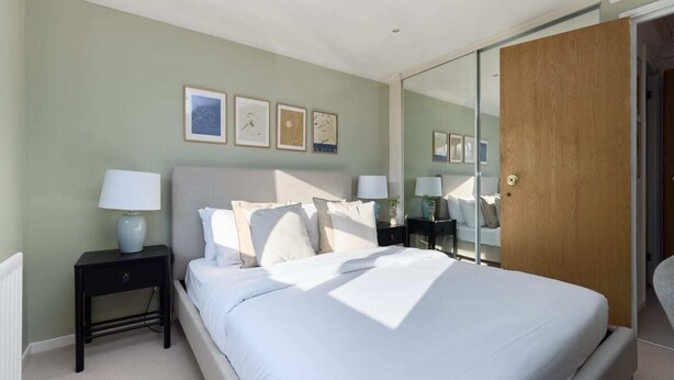 Un dormitorio con una cama, mesitas de noche, un espejo y cuadros en la pared.