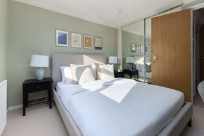 Un dormitorio con una cama, mesitas de noche, un espejo y cuadros en la pared.