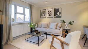 Una sala de estar moderna con un sofá, una mesita de centro y una silla. Hay tres cuadros enmarcados en la pared.