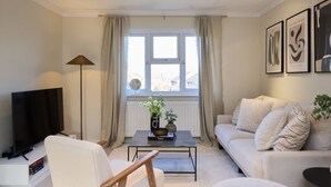 Una sala de estar con sofá, mesa de centro, televisor y ventana con cortinas.