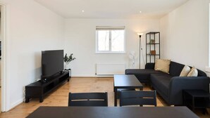 A modern living room with a flat-screen TV, a dark sofa, a coffee table, and a side table.