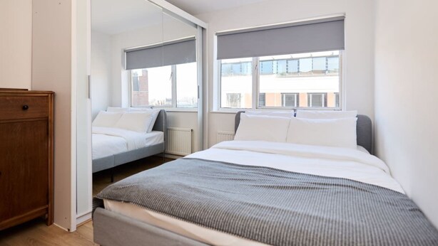 A modern bedroom with a large bed, a wooden dresser, and a wardrobe with a mirror.