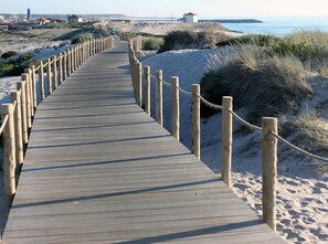 A wooden boardwalk leading to a beach with sandy dunes and a clear view of the ocean.
