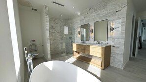 A modern bathroom with a freestanding bathtub, a wooden vanity with two mirrors, and a glass-enclosed shower area. - Buddy's Bungalow (Nassau)