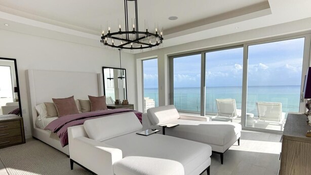 A modern bedroom with a large bed, a desk, and a view of the ocean. - Buddy's Bungalow (Nassau)