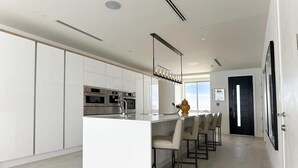 A modern kitchen with white cabinetry, a central island with bar stools, and a large window providing natural light. - Buddy's Bungalow (Nassau)