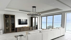A spacious living room with a large white sectional sofa, a flat-screen TV, and a modern chandelier. - Buddy's Bungalow (Nassau)