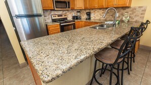 Una cocina con encimeras de granito, electrodomésticos de acero inoxidable, armarios de madera y una zona con taburetes de bar.