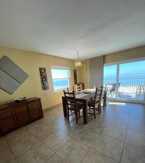 A dining area with a table and chairs, a chandelier, and a view of the ocean through a large window.