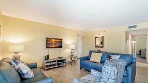 Una sala de estar con un sofá azul, un sillón estampado, un televisor y un cuadro en la pared.