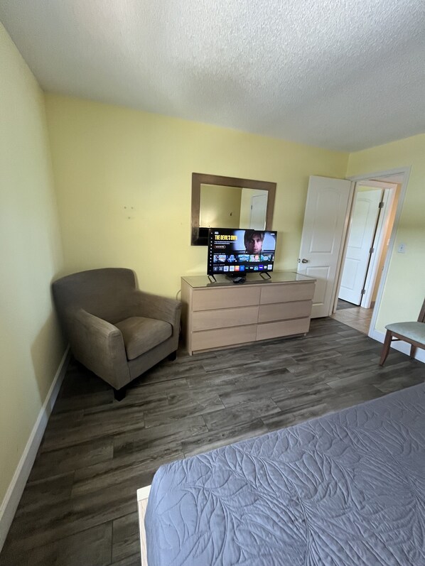 Un dormitorio con cama, cómoda, silla, televisor y puerta.