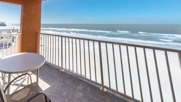 Un balcón con mesa y silla, con vista a una playa y olas.
