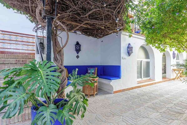 A covered outdoor seating area with a blue bench, potted plants, and a wall with decorative lanterns. - VILLA MARIA (Málaga)