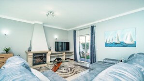 A modern living room with a fireplace, a flat-screen TV, and a large window with curtains. - Algarve Charm with Private Pool, Garden & Spacious Area in Lagos (Lagos)
