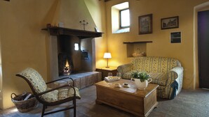 A cozy living room with a fireplace, a sofa, a chair, and a coffee table. - Farmhouse apartments with breathtaking scenery and unspoiled nature. (Umbria)
