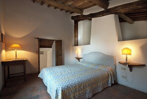 Ein Schlafzimmer mit einem Bett, zwei Nachttischen mit Lampen, einer Holztür und einem Steinfußboden.