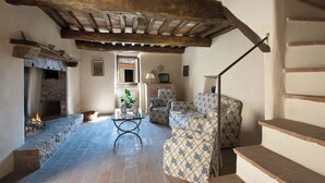 A rustic interior with exposed wooden beams, a stone fireplace, patterned furniture, and a staircase. - Farmhouse apartments with breathtaking scenery and unspoiled nature. (Umbria)