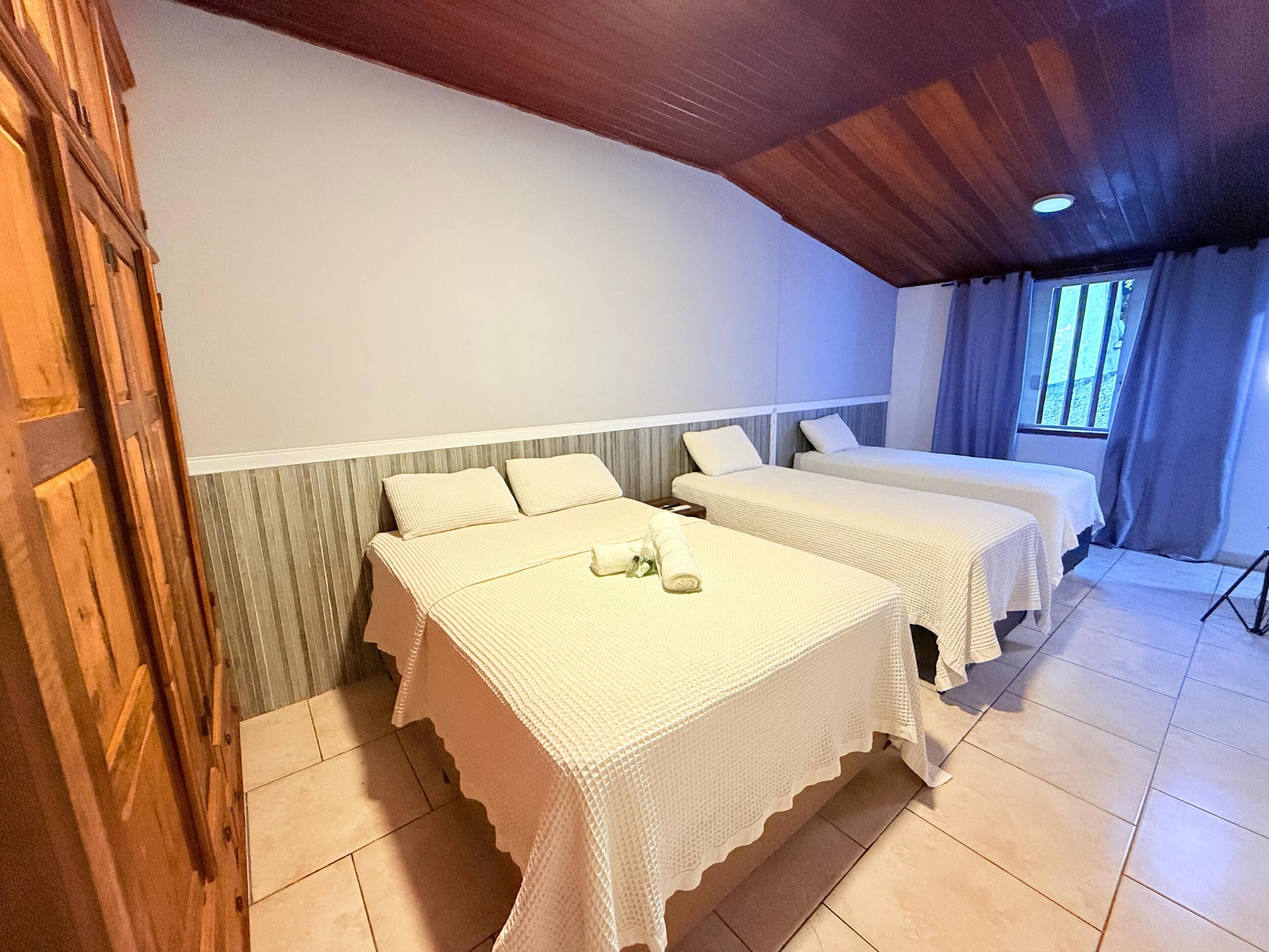 A room with two beds, a wooden ceiling, and a window with curtains.