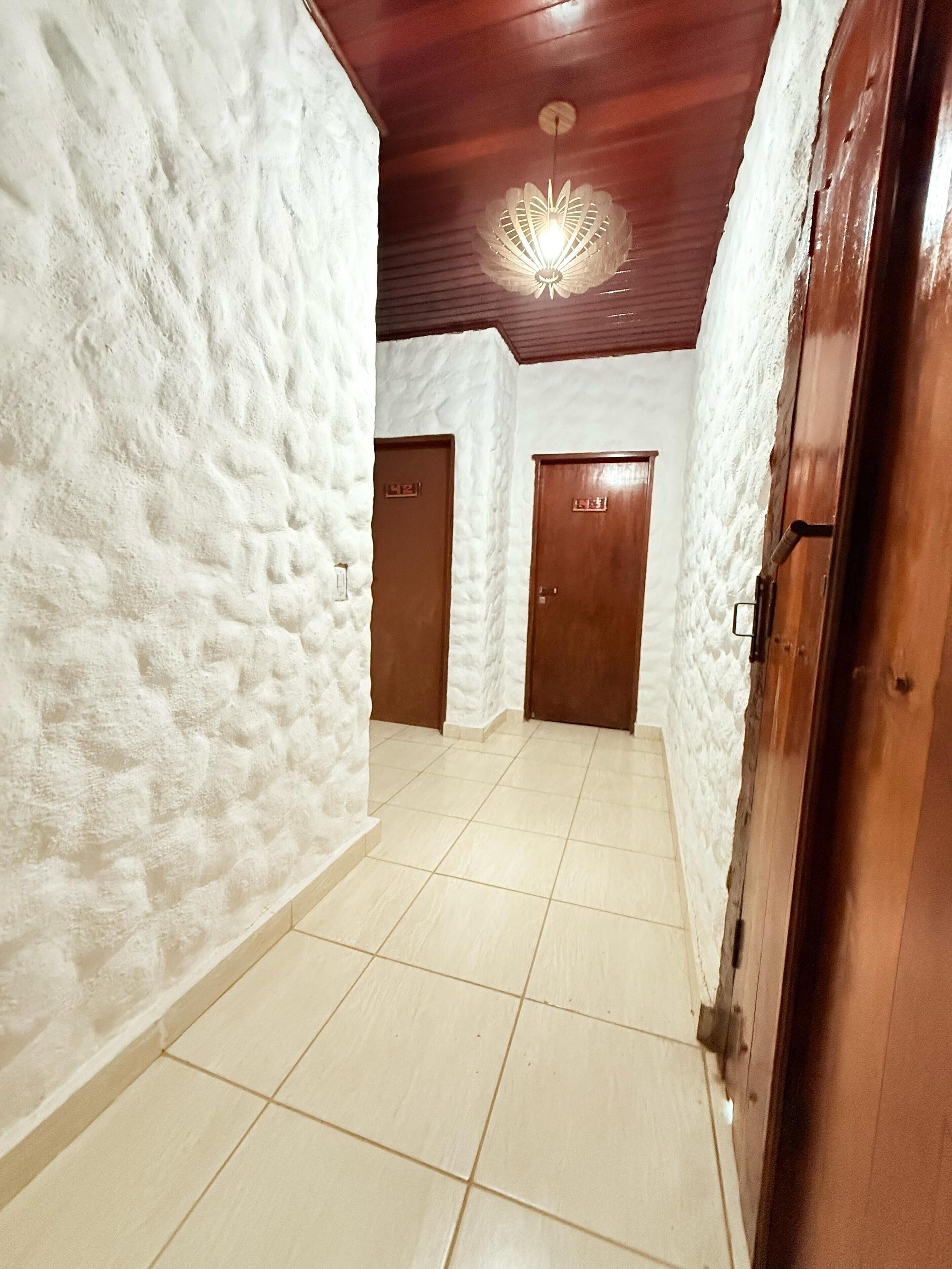 A hallway with white textured walls, wooden doors, and a tiled floor.
