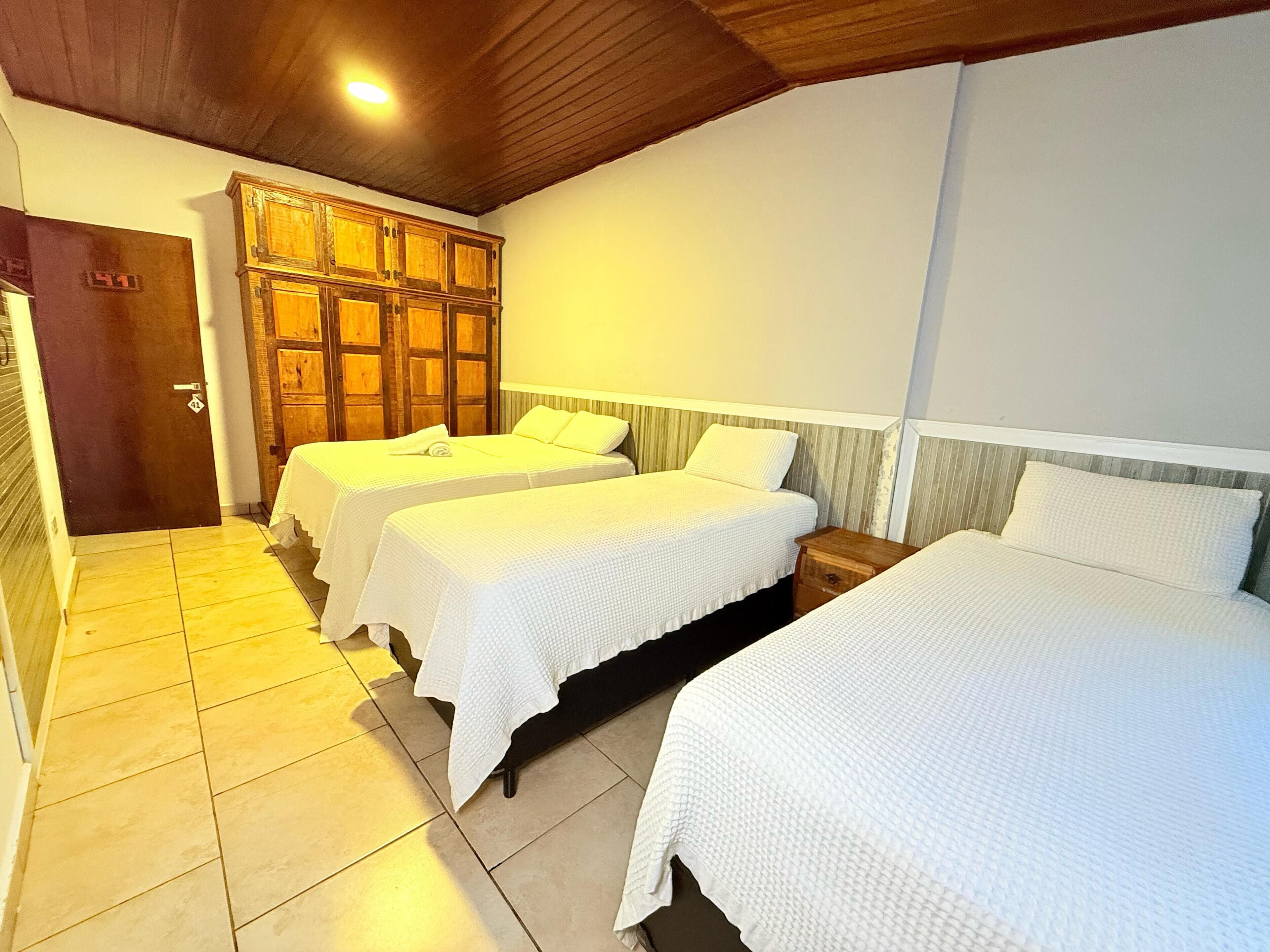 Habitación de hotel con tres camas individuales, armario de madera, suelo de baldosas y una puerta con un número.